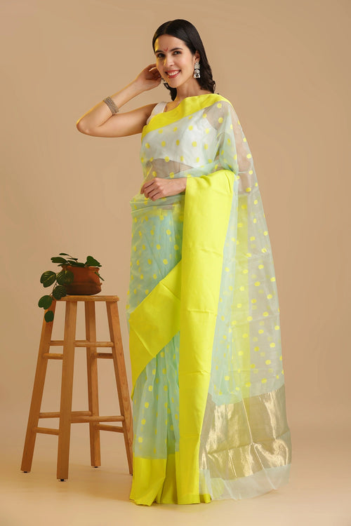 Full-length studio view of a model wearing the light blue handwoven Chanderi katan silk saree with yellow motifs and a neon yellow border, styled with traditional silver jewelry