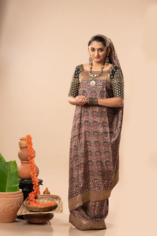 Full-length studio view of a model wearing the warm brown Autumn Whisper Ajrakh Dola silk saree with golden patterned border and natural block-printed details