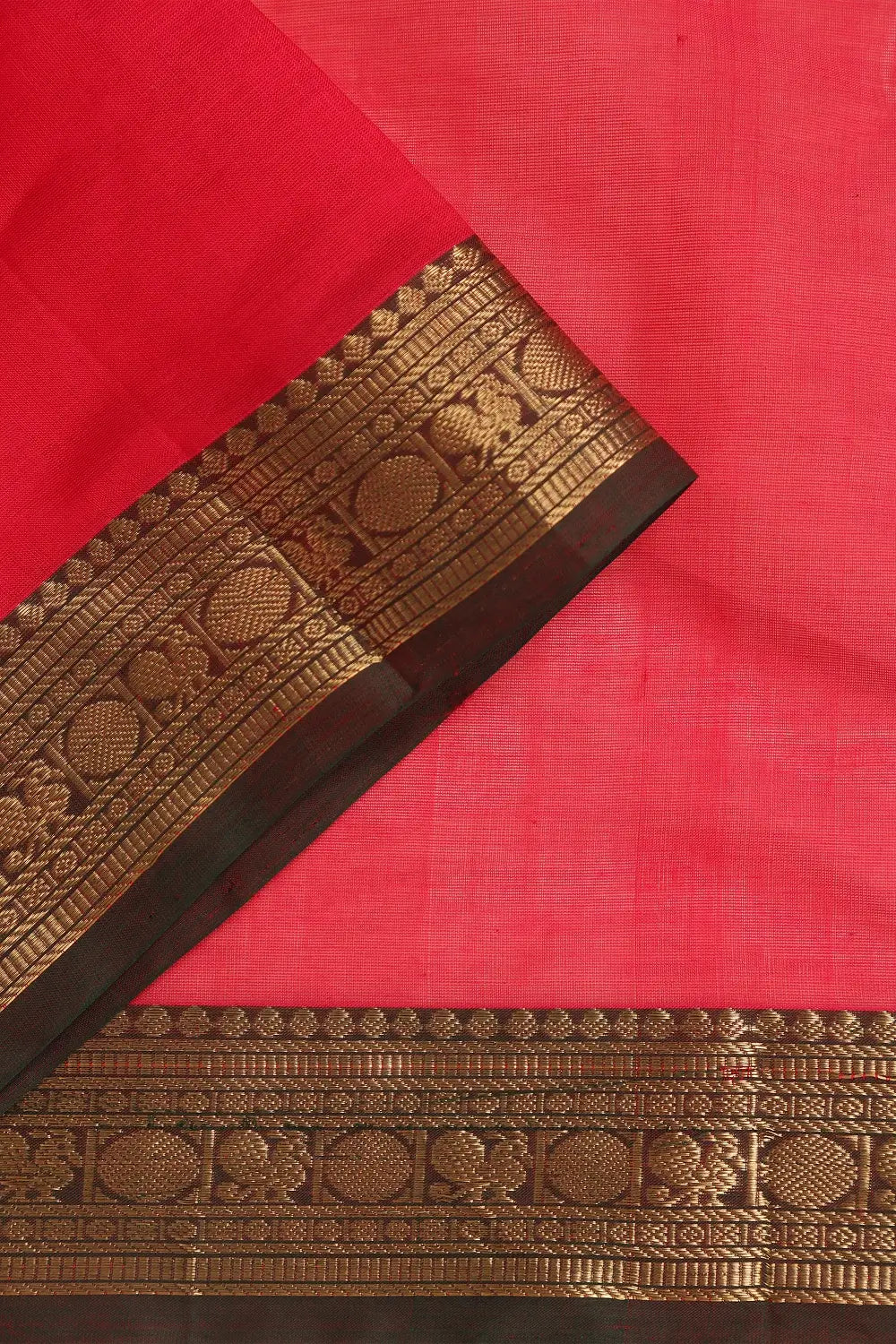 Close-up view of the intricate traditional dark border folded over the red silk-cotton fabric