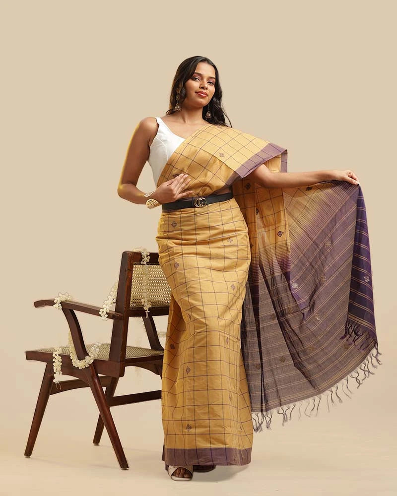 Standing studio view showcasing the full drape, checked weave, and purple pallu of the golden ochre Kasaragod handloom saree