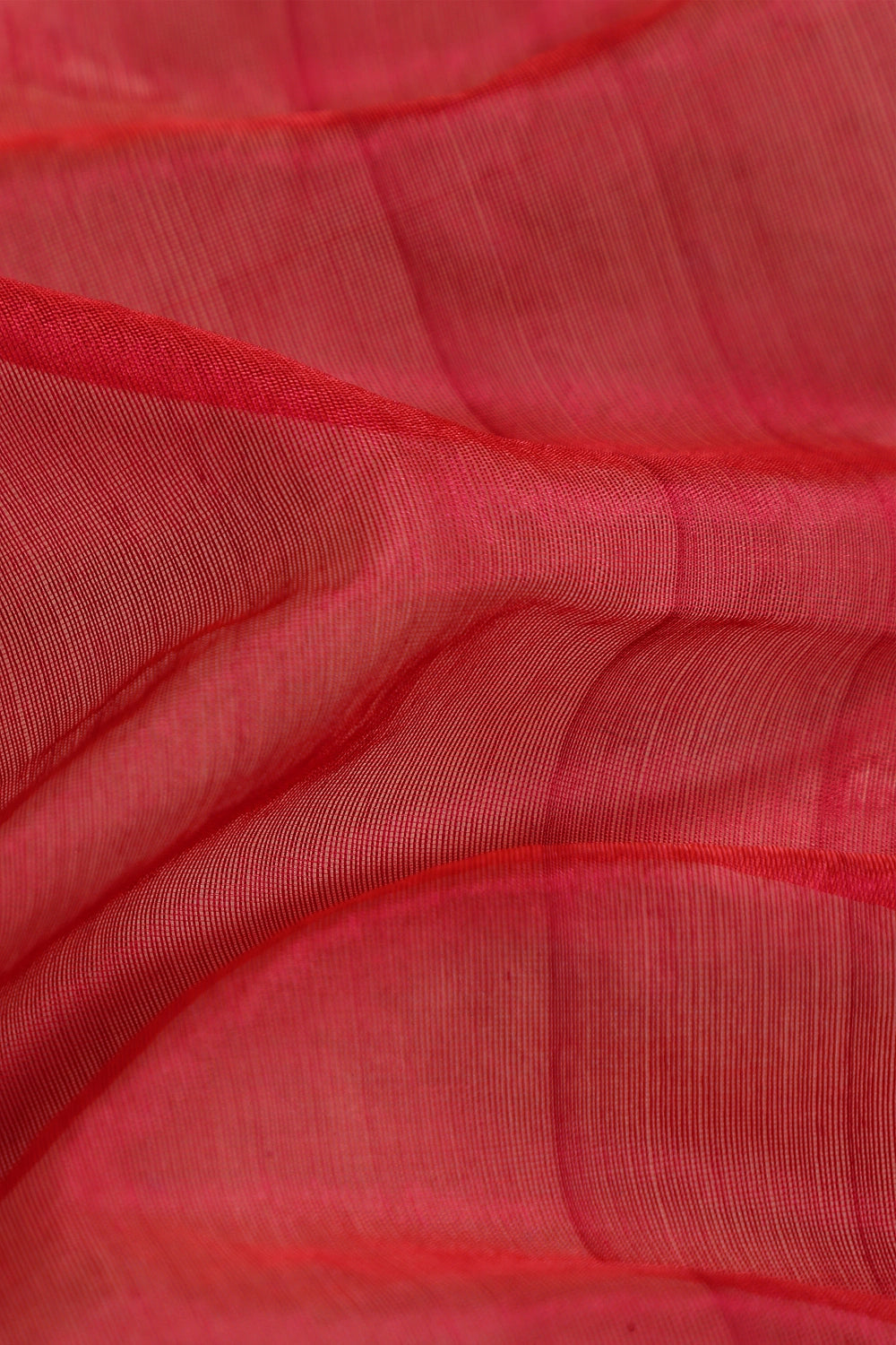 Close-up view of the folded bright red pattu silk fabric highlighting its lustrous texture and fine golden zari weave
