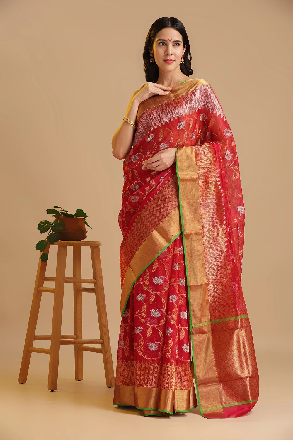 Full-length studio view of a model wearing the bright red handwoven Chanderi pattu silk saree with golden zari weave and bell motifs, styled with traditional silver jewelry