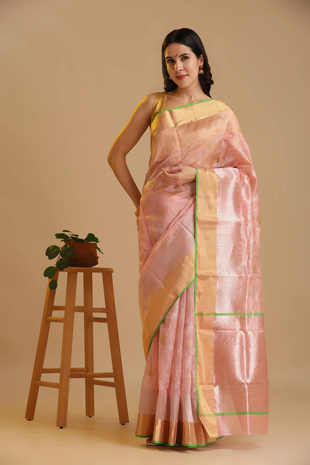Full-length studio view of a model wearing the soft blush pink handwoven Chanderi pattu silk saree with golden zari weave and bell motifs, styled with traditional silver jewelry