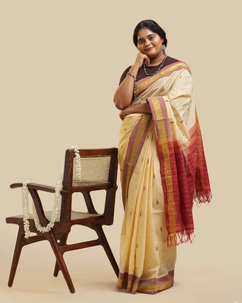 Standing studio shot displaying the full silhouette, length, and rich maroon pallu end of the ivory cotton Kasaragod saree