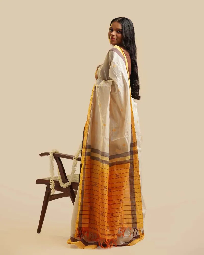Rear full-length view of a model displaying the back silhouette, draped pleats, and vibrant mustard pallu of the ivory cotton saree