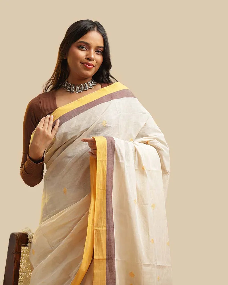 Close-up upper body view of a model wearing the ivory mist Kasaragod cotton saree featuring a mustard border and delicate buti motifs, paired with a brown blouse