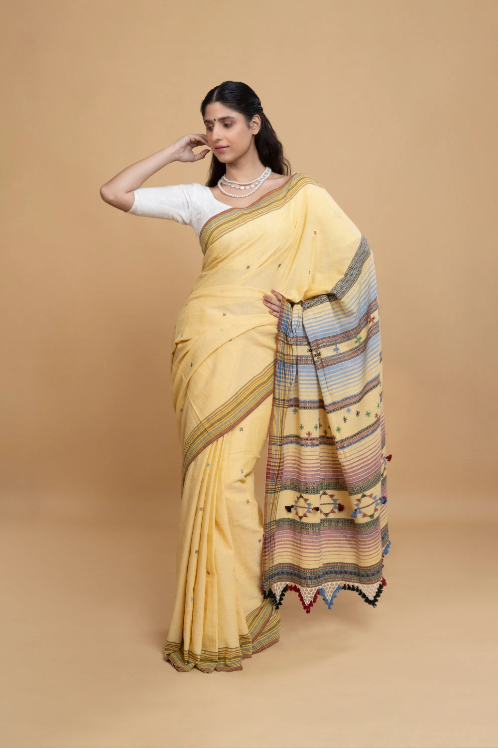 Full-length studio view of a model wearing a butter yellow pure handloom cotton Bhujodi saree paired with a contrasting white blouse, featuring a pastel stripe pallu and tassel fringe
