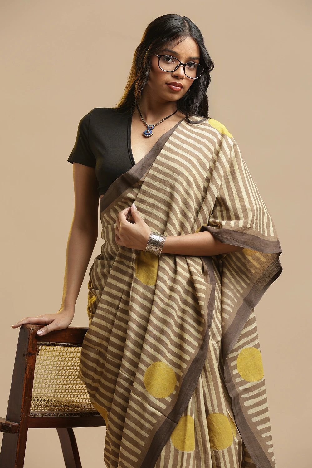 Model posing in the beige and brown striped Bagru cotton saree against a neutral studio backdrop