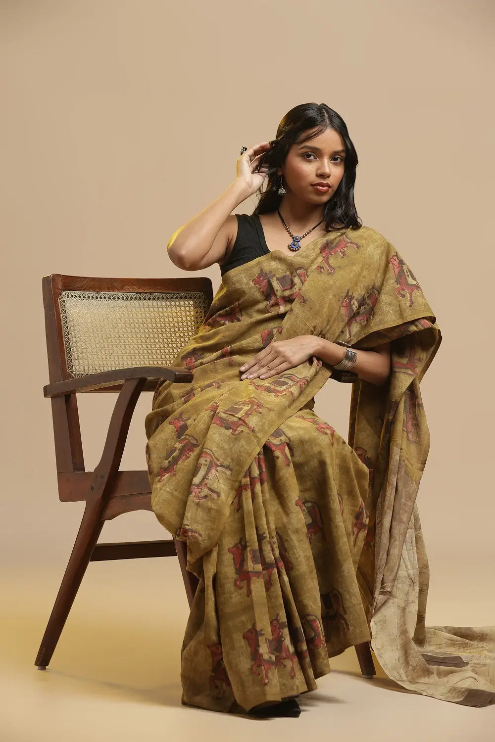 Mustard yellow handblock print cotton saree featuring traditional Bagru cow motifs displayed by a model seated beside a wooden chair