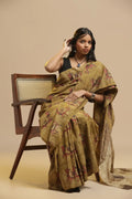 Mustard yellow handblock print cotton saree featuring traditional Bagru cow motifs displayed by a model seated beside a wooden chair