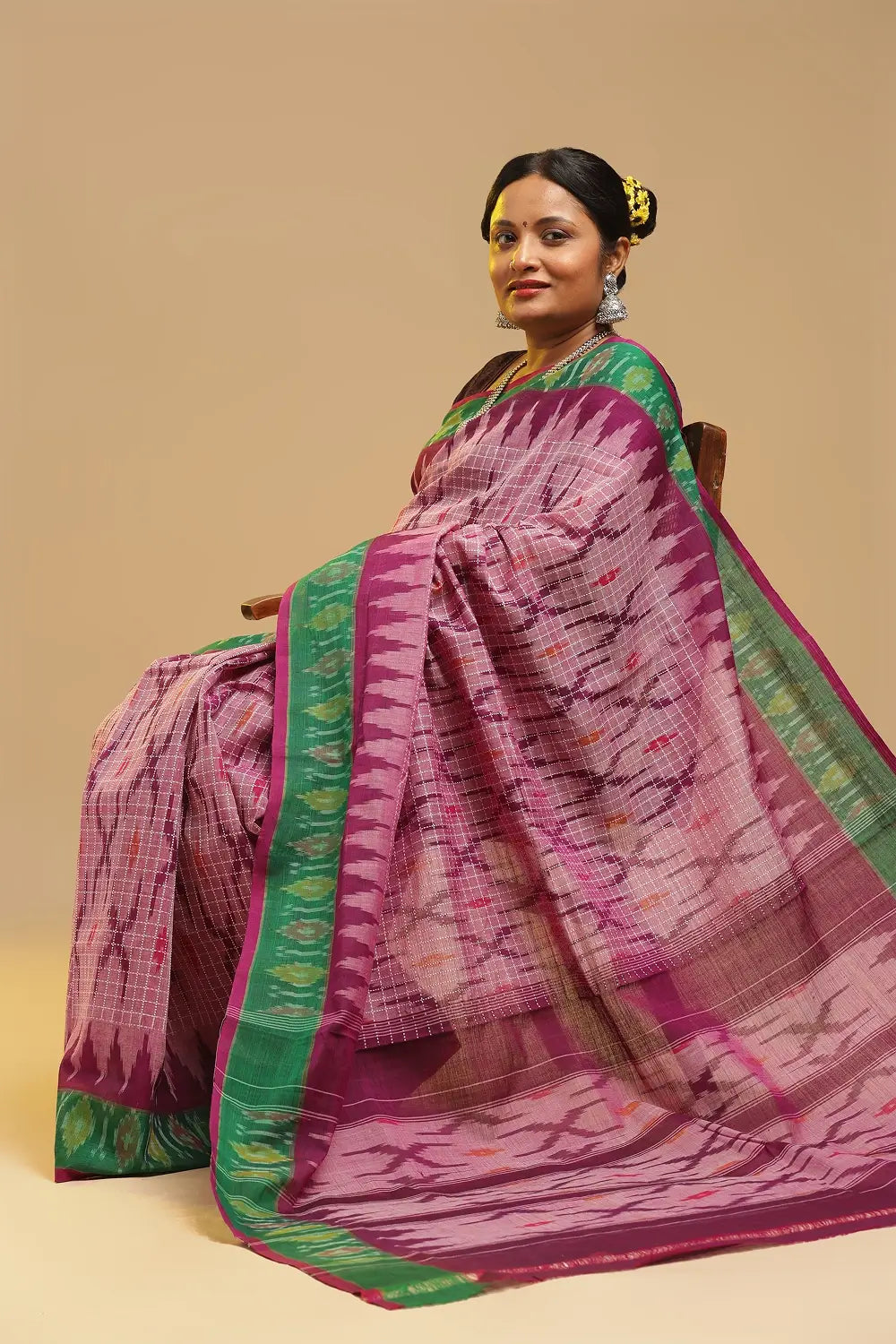 Bright pink and green Muthyampet check cotton saree featuring single ikat patterns and temple design panel displayed by a seated model