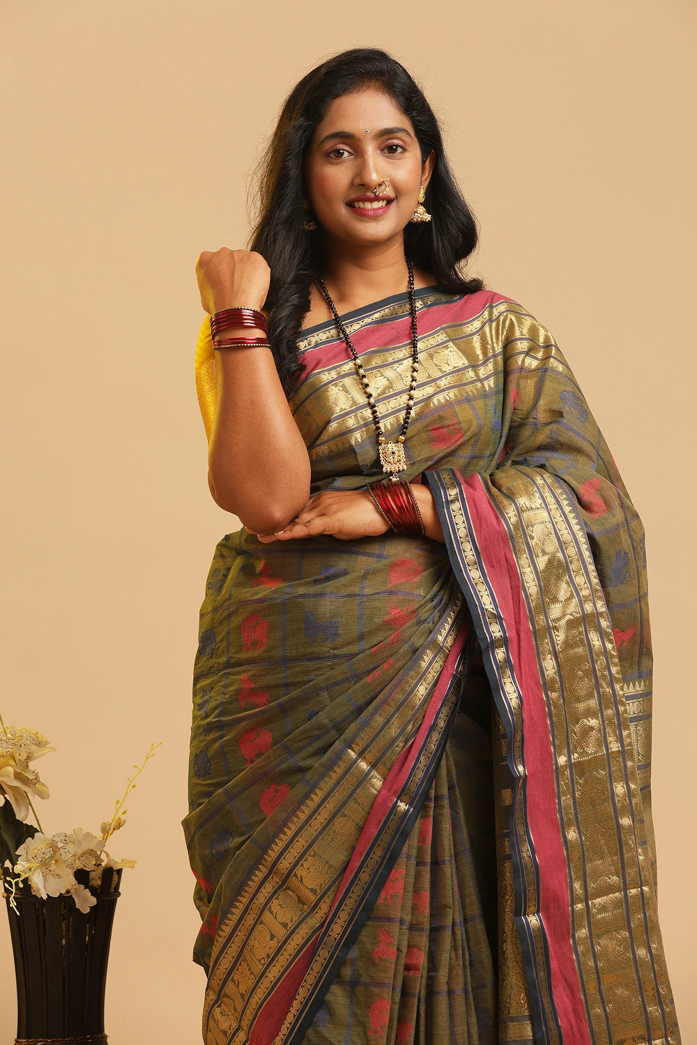 Model posing gracefully in the earth green Kanchipuram handloom cotton saree against a neutral studio backdrop