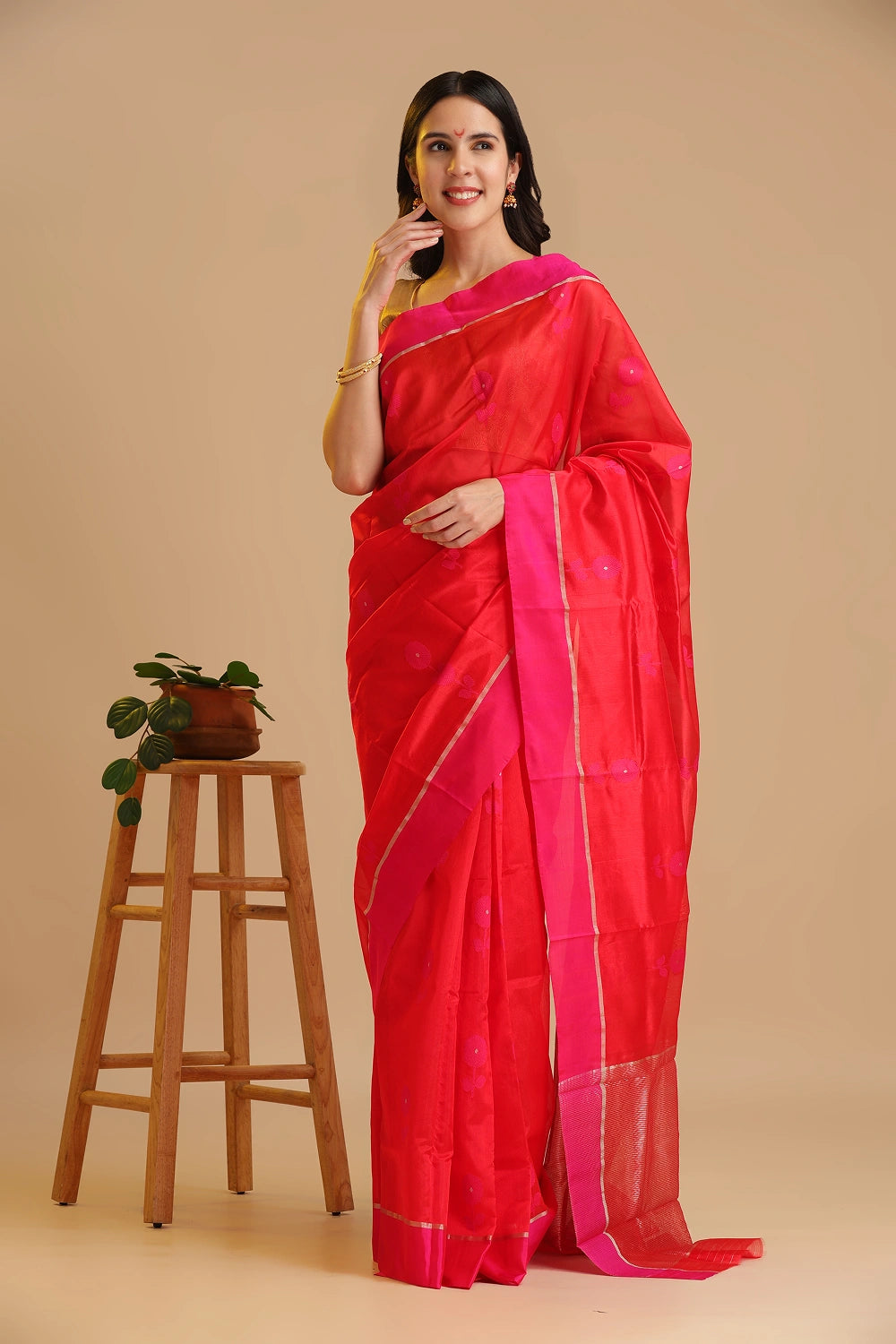 Full-length studio view of a model wearing the bright orange handwoven Chanderi pattu silk saree with a pink border and floral motifs, styled with traditional silver jewelry