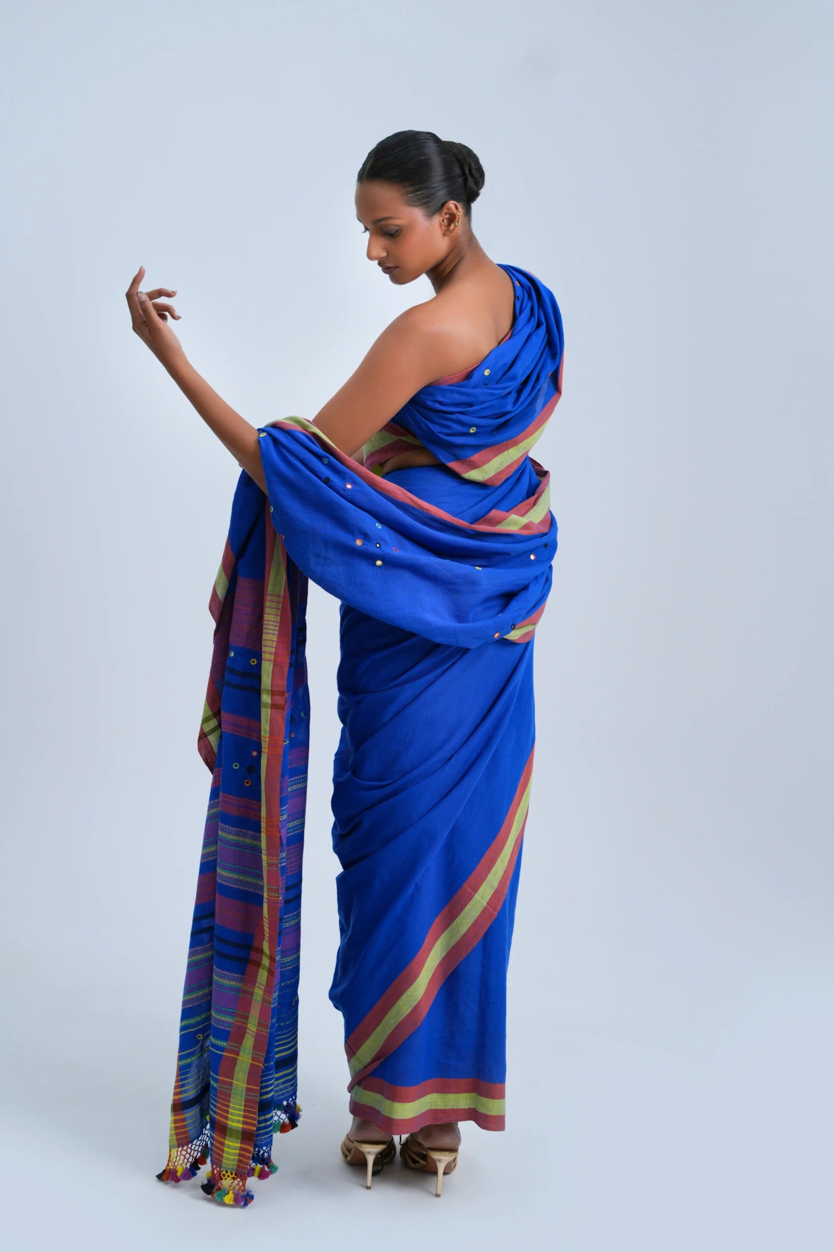 Rear full-length view of a model highlighting the back silhouette, draped pleats, and multicolour pom-pom fringe pallu