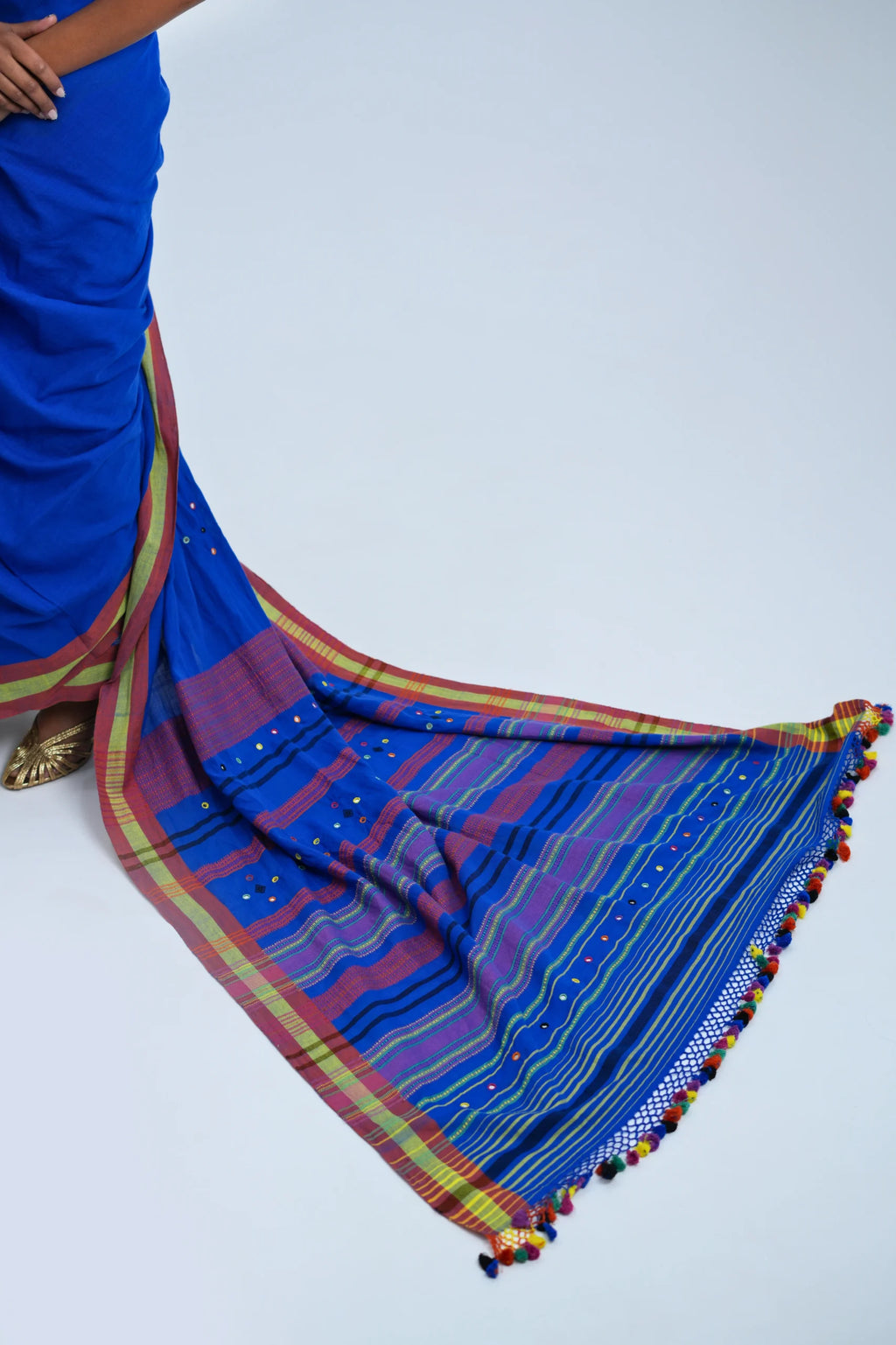 Detailed close-up of the richly layered horizontal stripe pallu, crochet-lace edge, and multicolour pom-pom tassel fringe