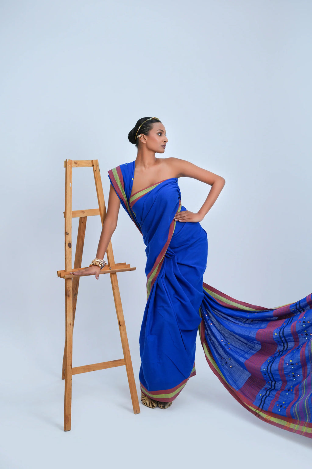 Studio action shot of a model posing next to a wooden ladder, highlighting the fluid movement and rich colors of the Bhujodi saree