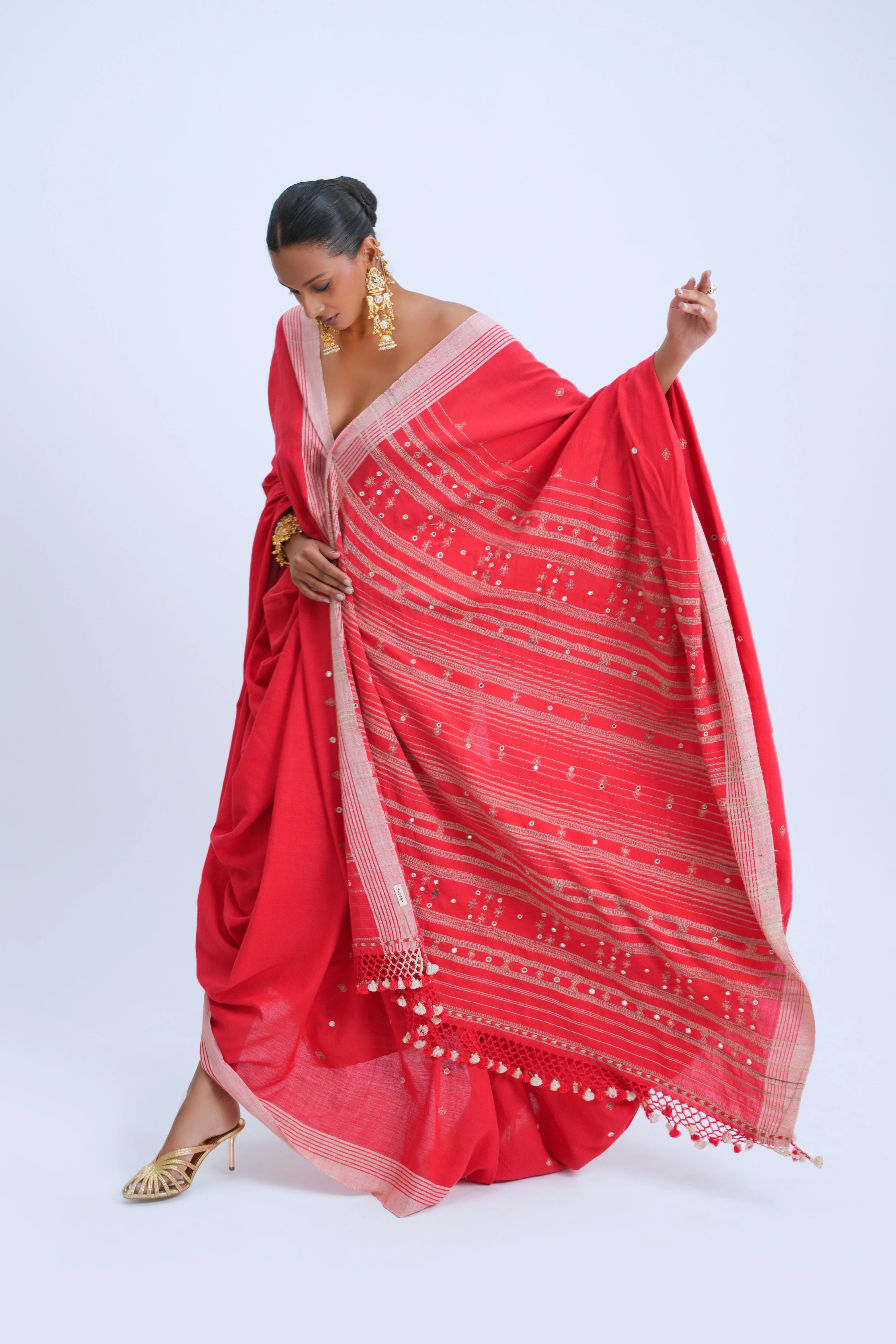 Studio action shot highlighting the fluid drape, vibrant scarlet hue, and detailed golden pallu of the Bhujodi saree