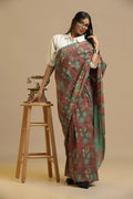 Shades of Earth brown and green handblock print cotton saree displayed by a model posing beside a wooden stool