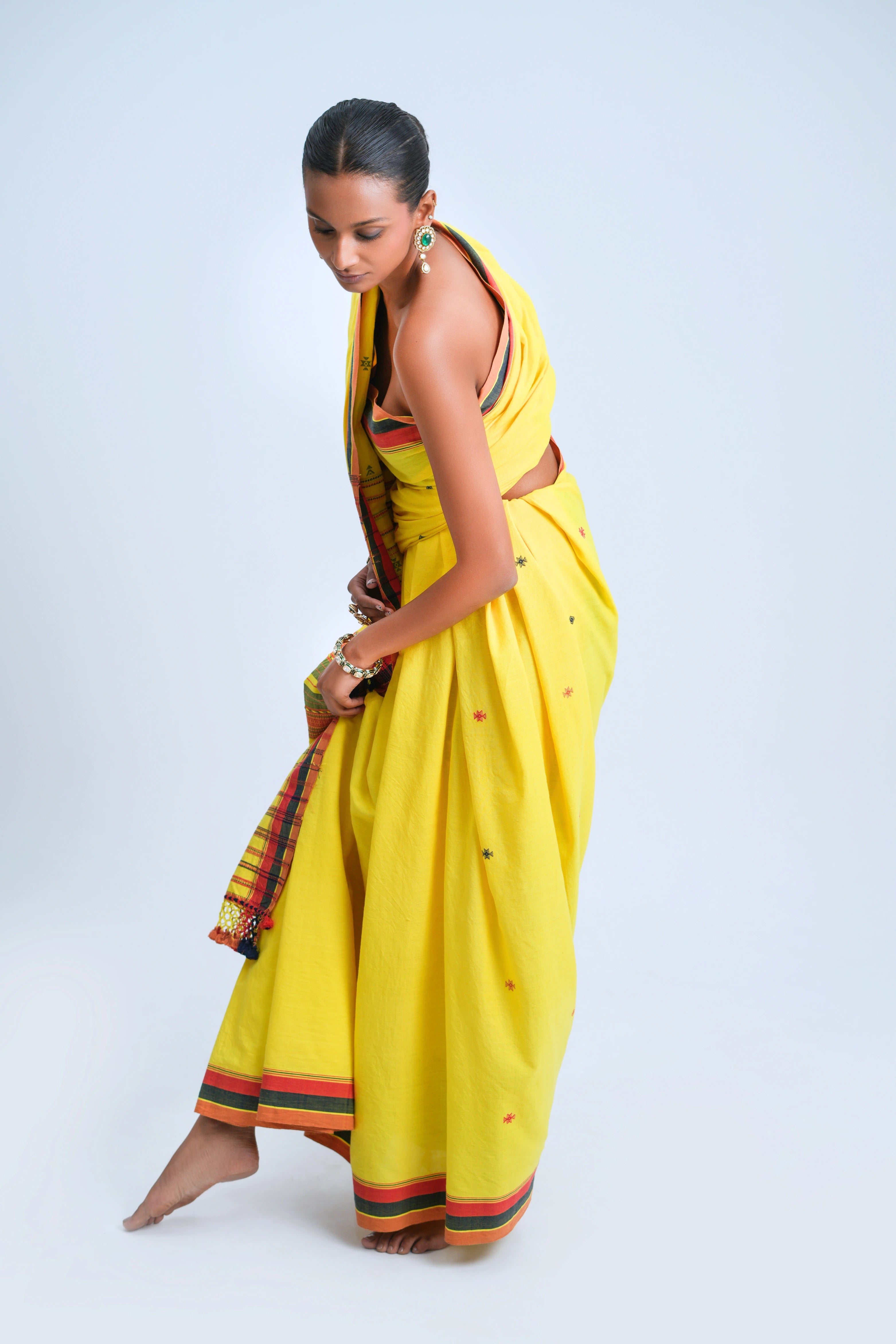 Model adjusting the graceful pleats of the sunshine-yellow Bhujodi saree in a studio setting