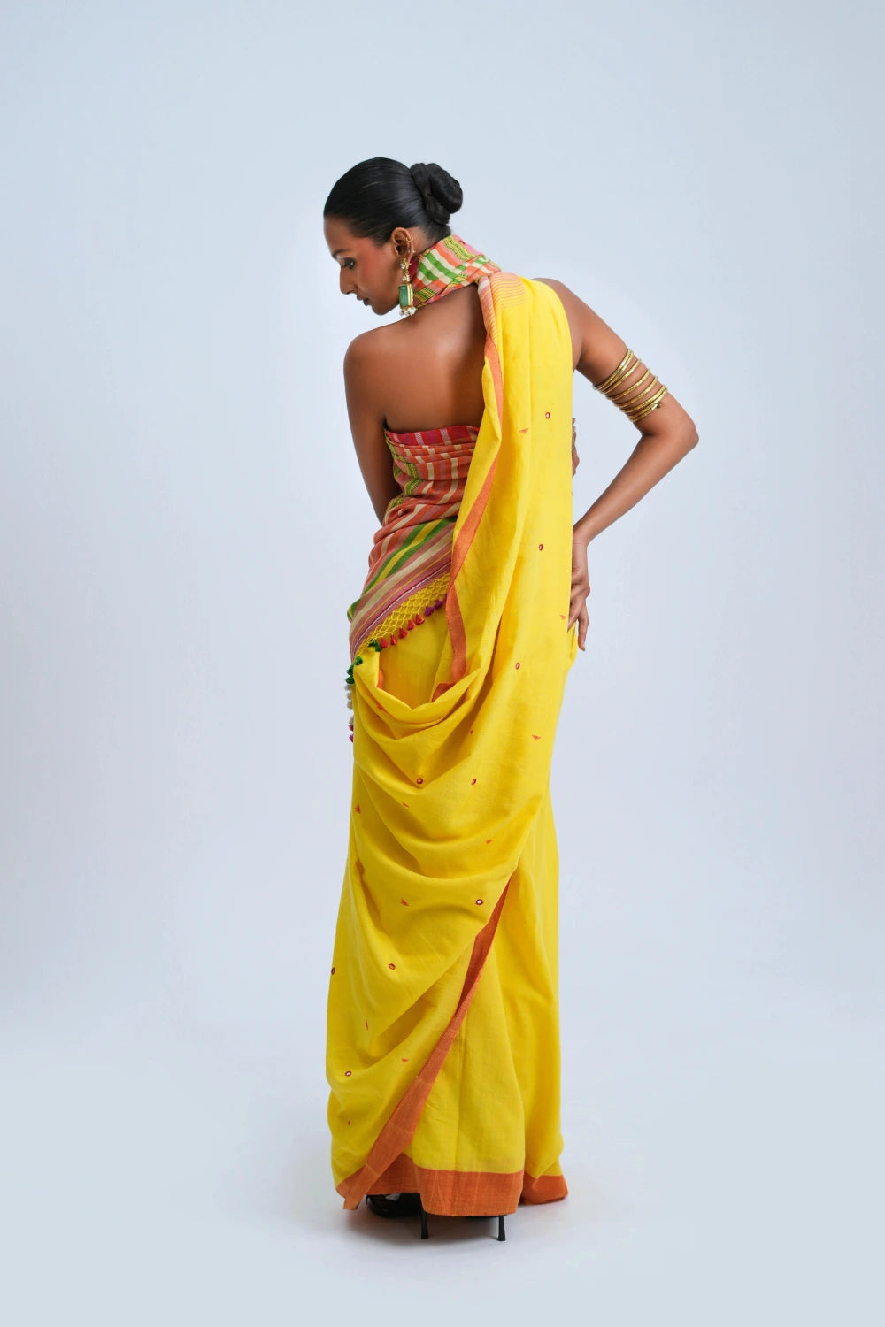 Rear full-length view of a model displaying the graceful fall, draped pleats, and finished border of the sunshine yellow Bhujodi saree