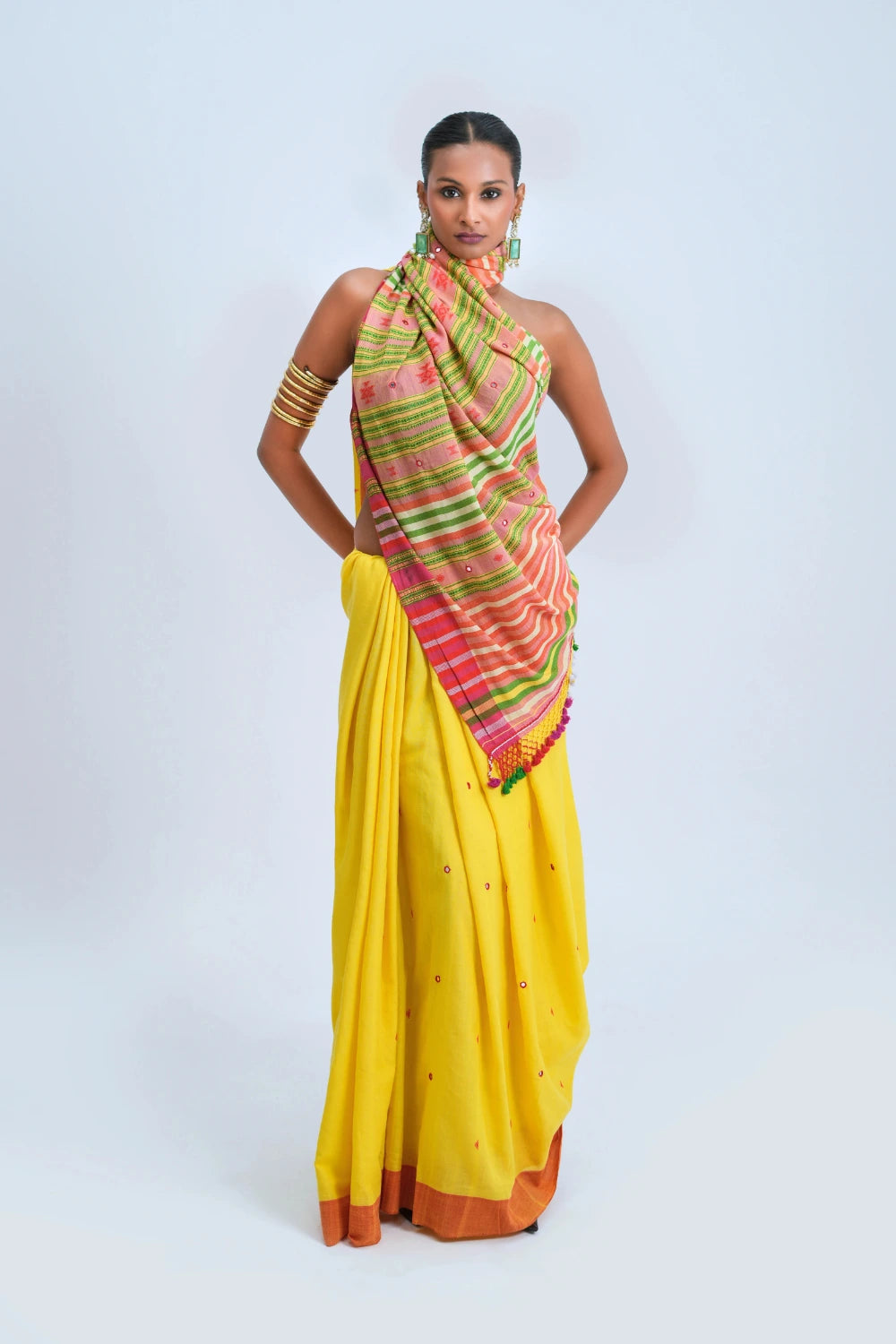 Full-length studio view of a model wearing a sunshine yellow pure handloom cotton Bhujodi saree featuring a burnt orange-rust border and vibrant multicolour stripe pallu