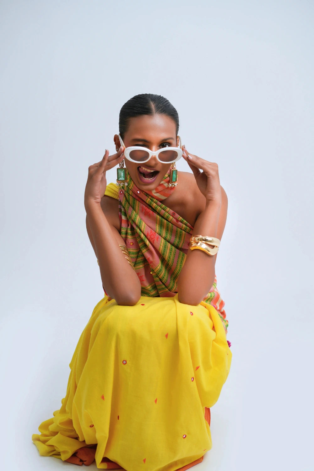 Seated playful studio view highlighting the rich color contrast, draped pallu, and festive styling of the Bhujodi saree