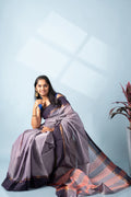 Seated studio view of a model wearing the lavender-grey Twilight Aura Kodiyala cotton saree with violet-navy border and rust-toned striped accents