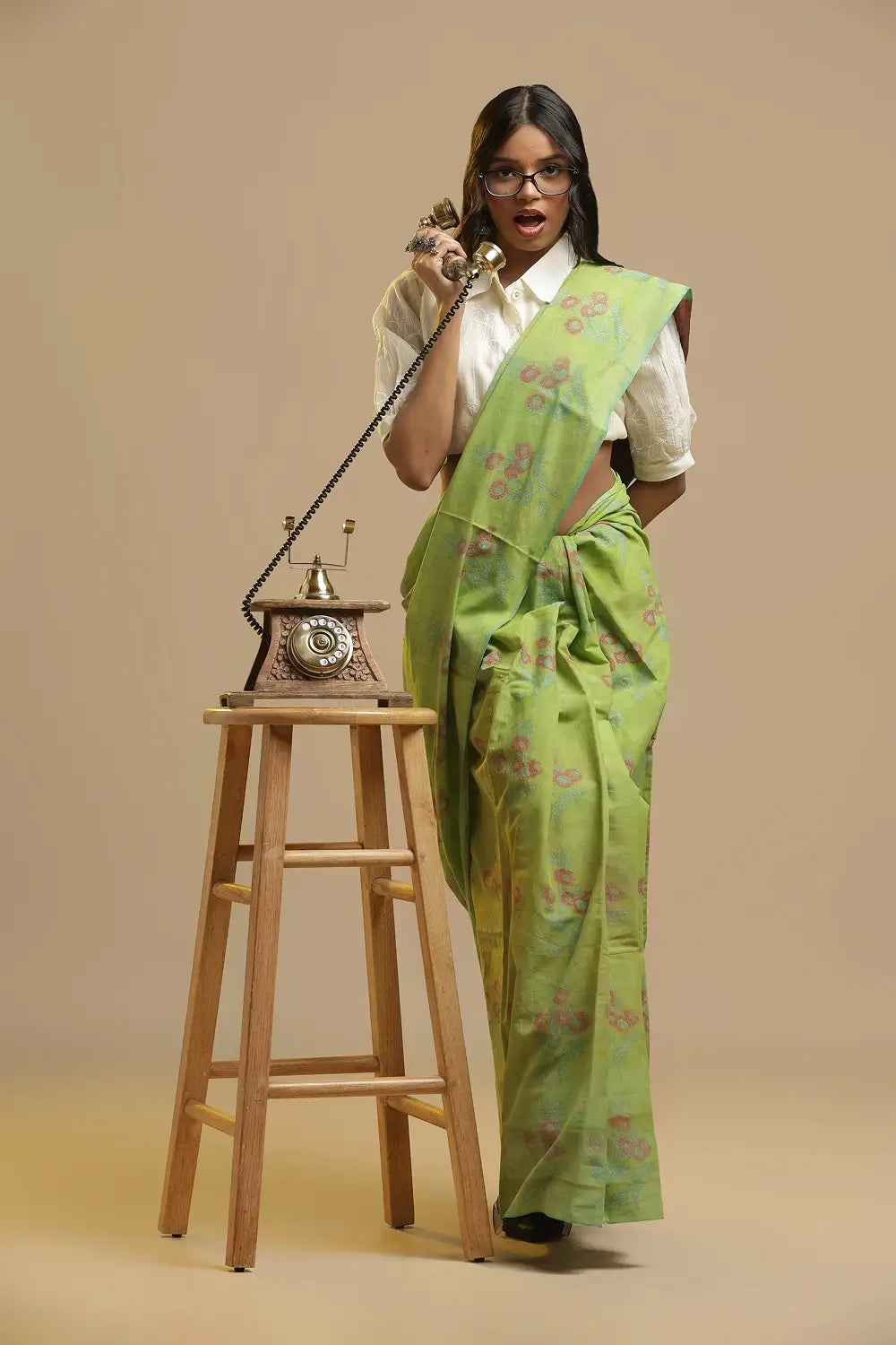 Vibrant lime green handblock print cotton saree with floral motifs displayed by a model posing with a vintage telephone on a wooden stool